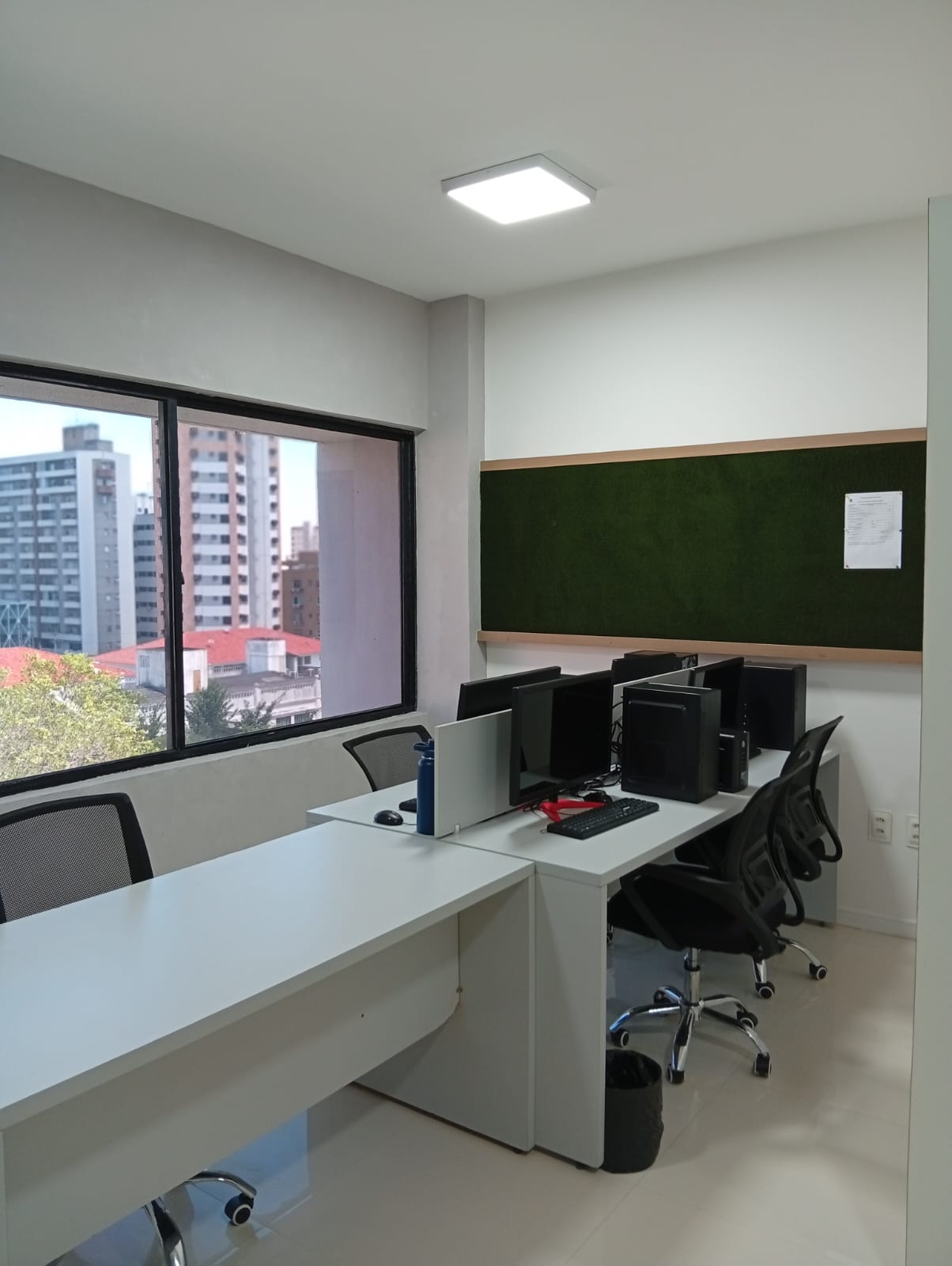 Área de trabalho com computadores e mesas próximas à janela